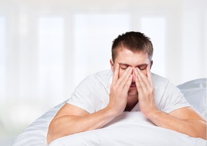 Man lying on stomach in bed rubbing his eyes