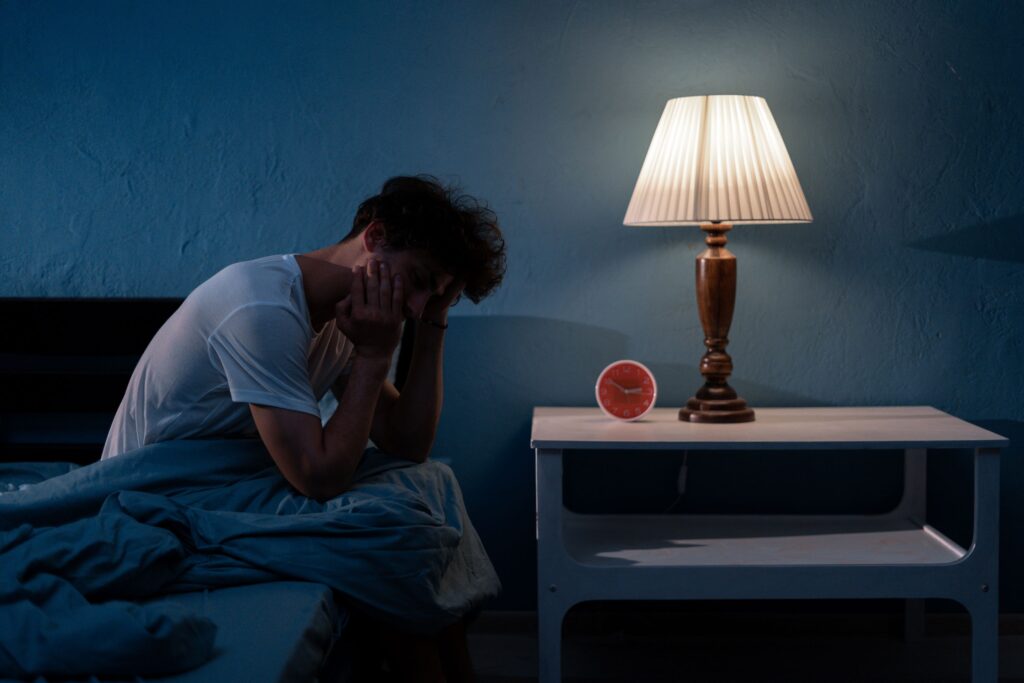 Man in bed holding hand to head restlessly with lamp on